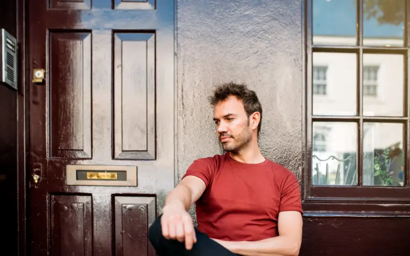 Locked Out of Your House,A man locked out of his house, sitting on a bench outside a building, waiting for assistance